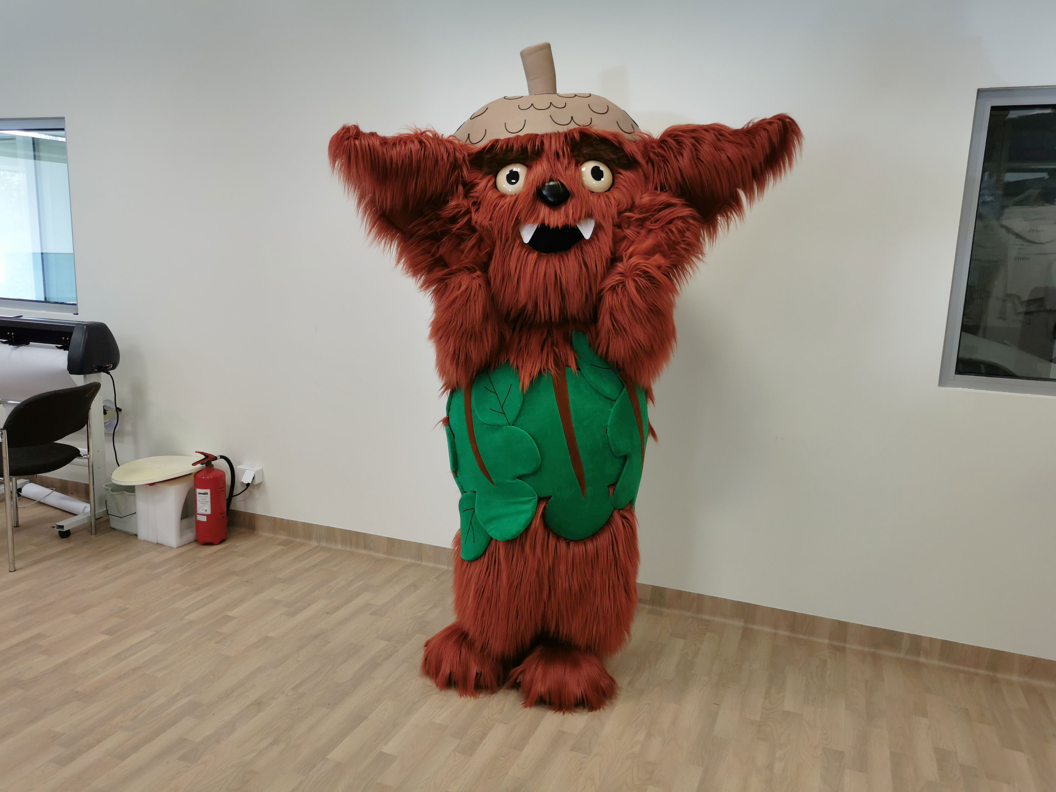 Na fotografii widnieje strój reklamowy w postaci ludzika stworka skrzata leśnego pozujący do zdjęcia przed siedzibą firmy Elabika